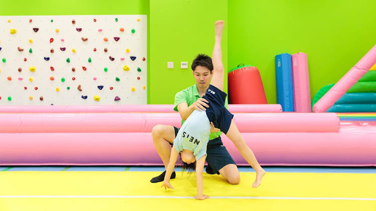 バク転の練習の一環として側転を練習する子どもと補佐する講師